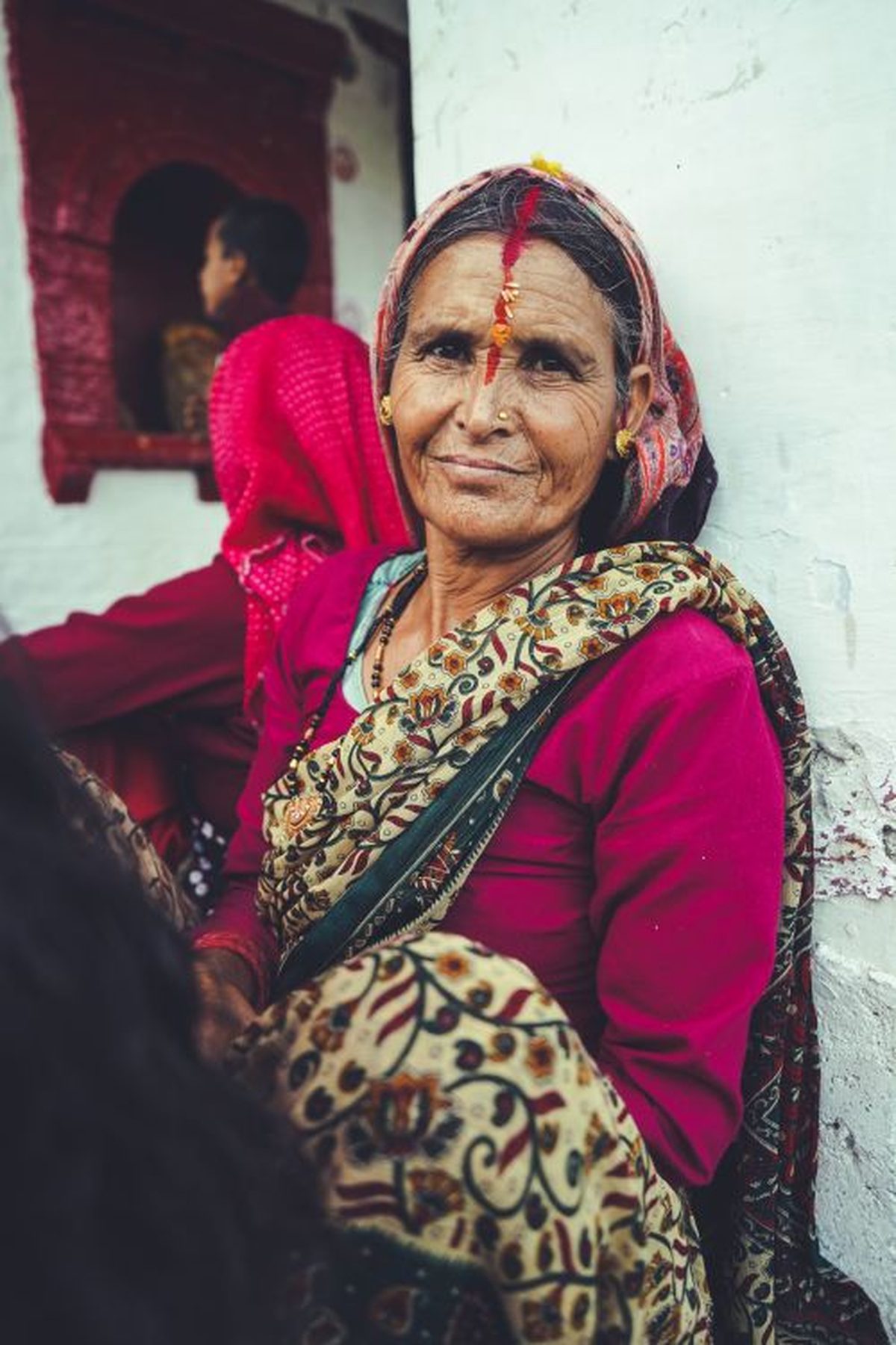 An elderly Indian woman in a pink saree smiling