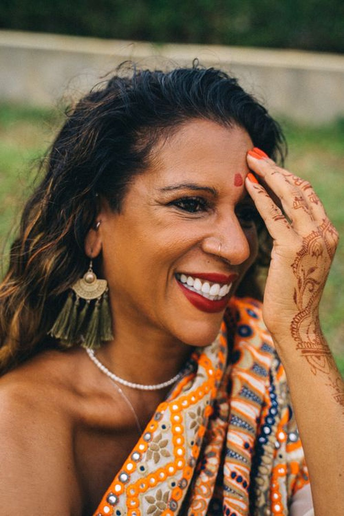 A smiling Indian woman in an orange saree with mehndi on her hand